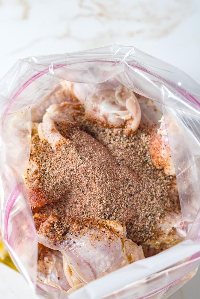 Close up image of wings in a gallon bag with seasonings on top. 