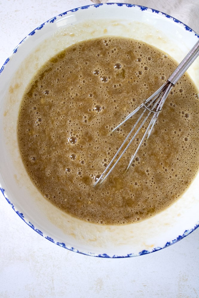 Mashed bananas with sugar and oil in a bowl with a whisk.