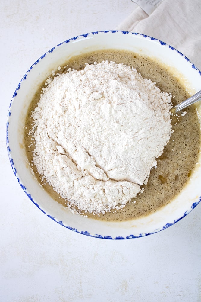 Wet banana cake batter with dry ingredients on top in a bowl.