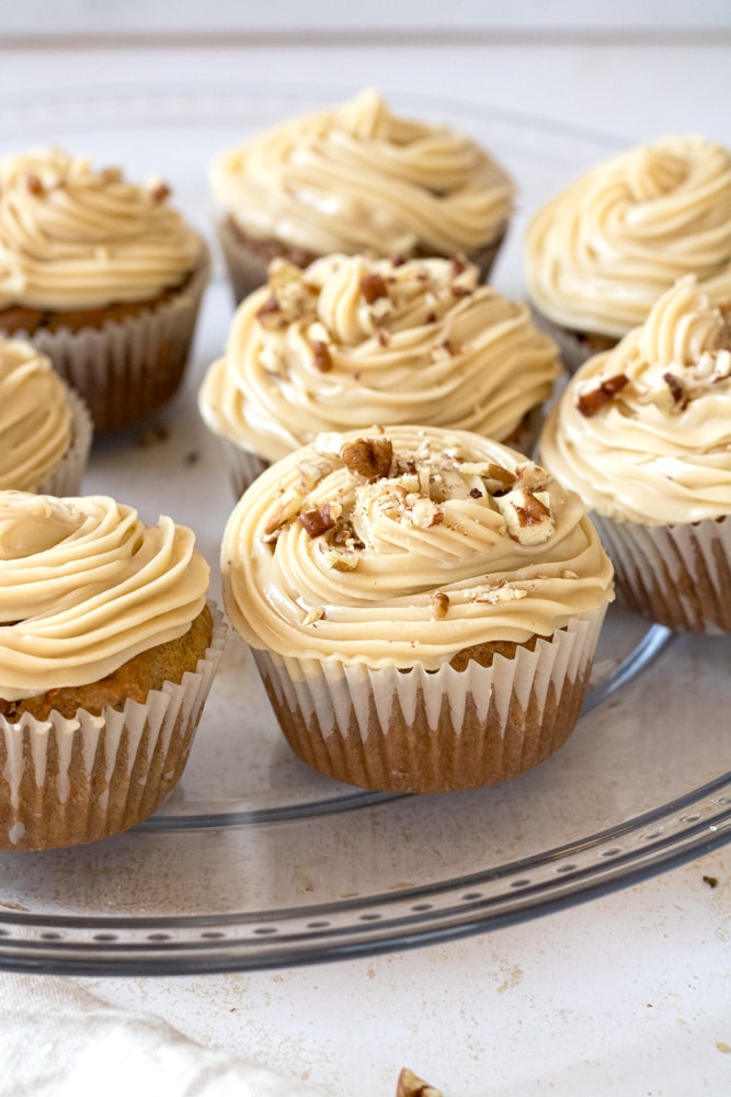 Carrot cake cupcakes on a plate with chopped nuts on top.