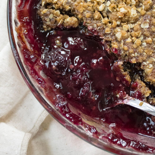 Close up image of cherry crisp in a pie pan with a spoon.