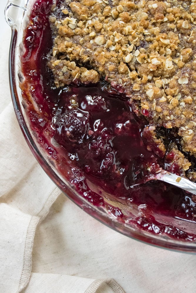 Close up image of cherry crisp in a pie pan with a spoon.