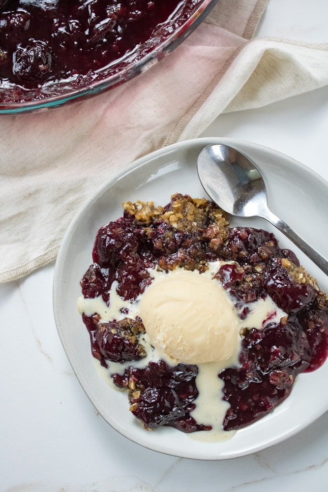 Overhead image of cherry crisp with a melty scoop of ice cream on top.