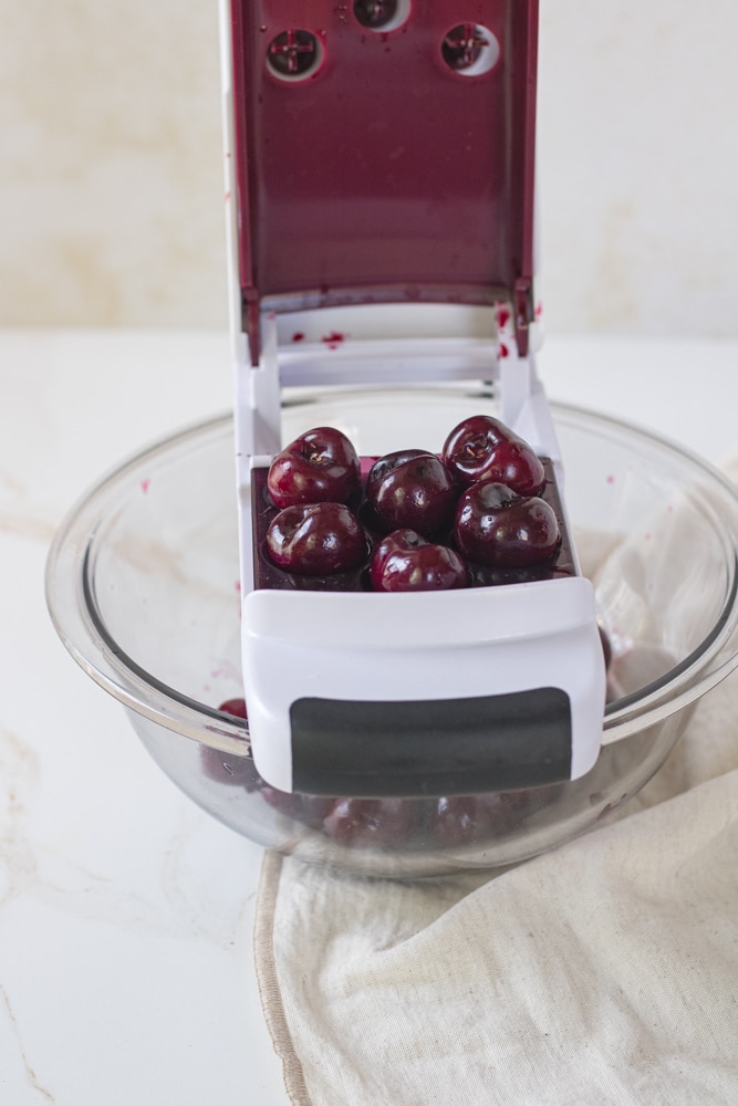Cherry pitter set over a bowl with cherries in it.