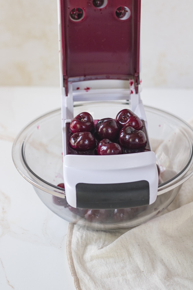 Cherry pitter set over a bowl with cherries in it. 