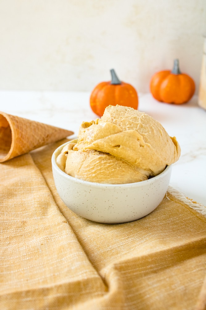 Pumpkin spice ice cream in a bowl with cone near by.