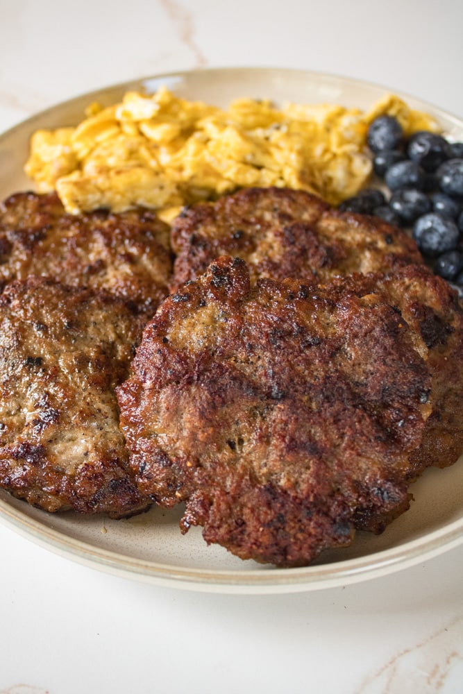 Close up image of turkey sausage patties on a plate with eggs and blueberries.