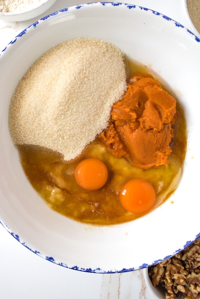 Sugar, eggs, pumpkin puree, and mashed bananas in a bowl.