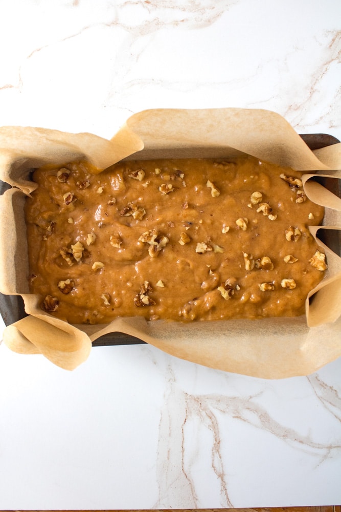 Banana mixture in a loaf pan with nuts on top.