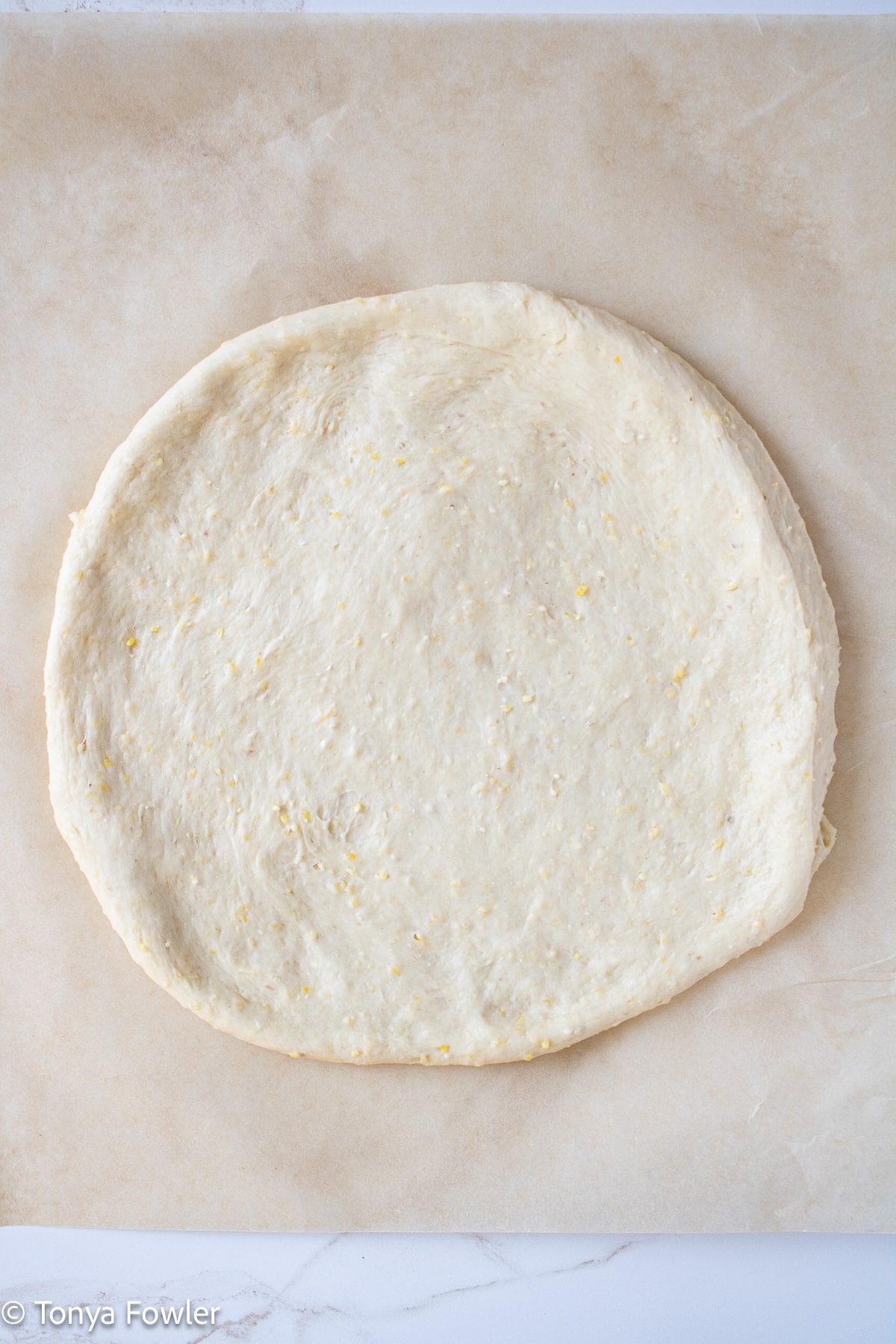Pizza dough spread out on parchment paper.