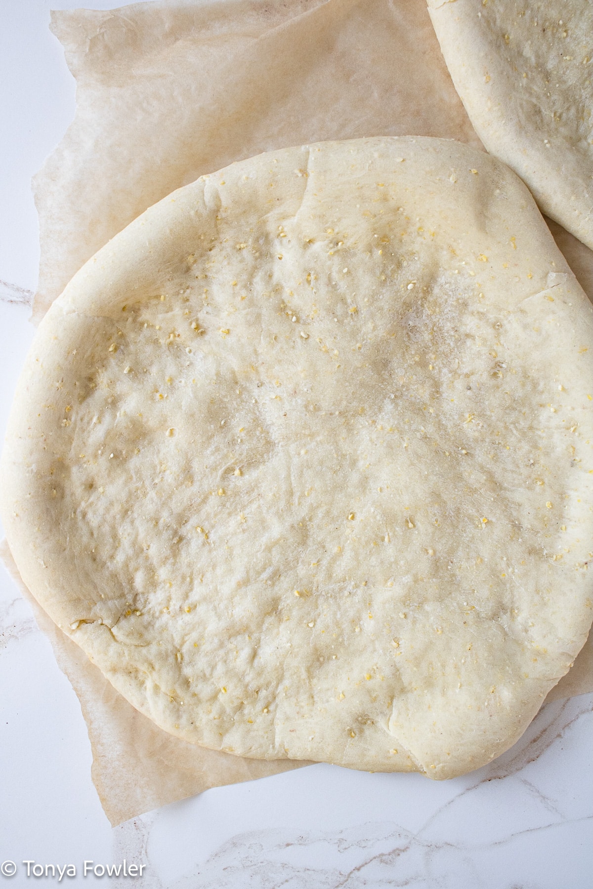 Cornmeal pizza crust on a parchment paper.