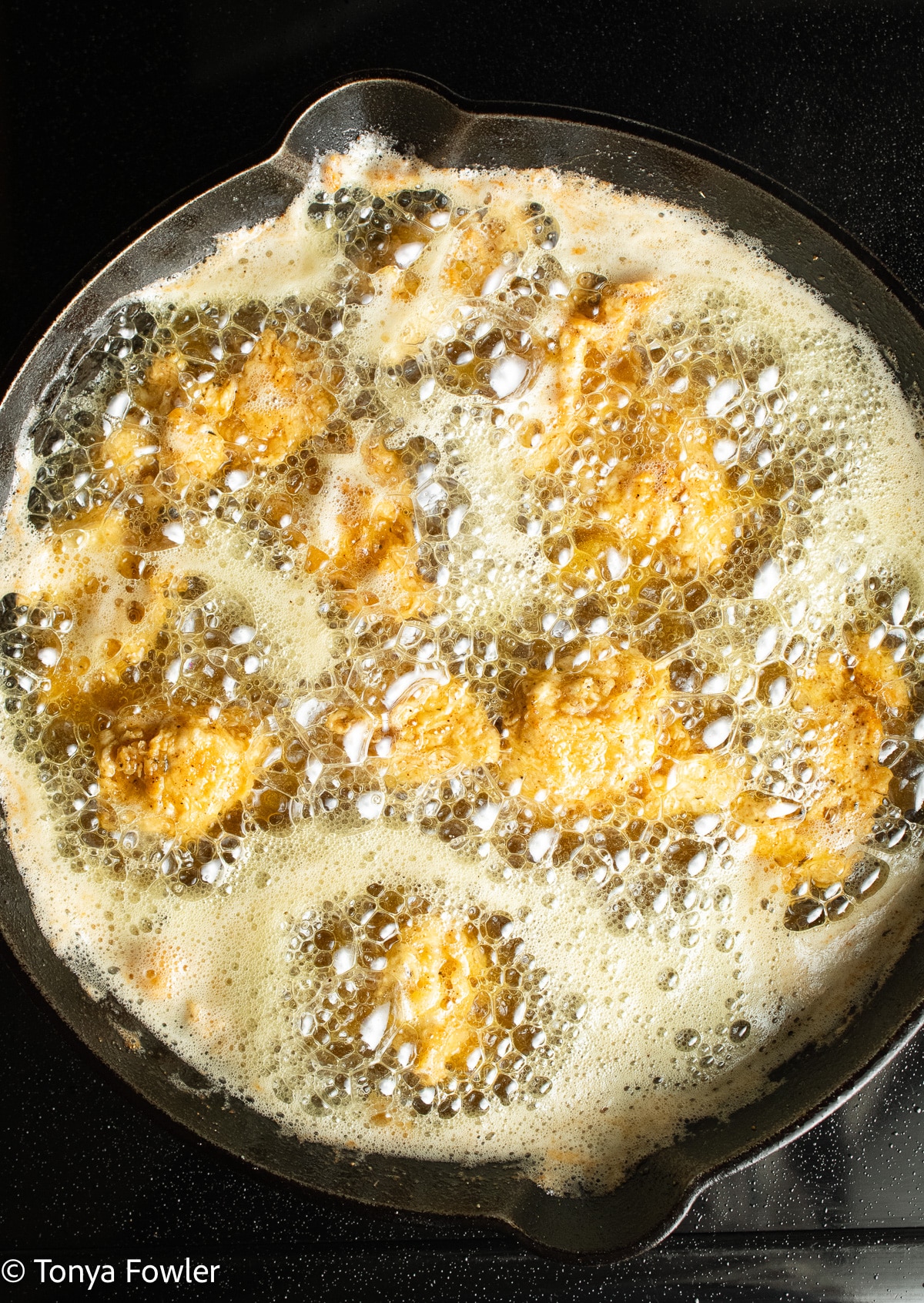 Chicken frying in a cast iron skillet.