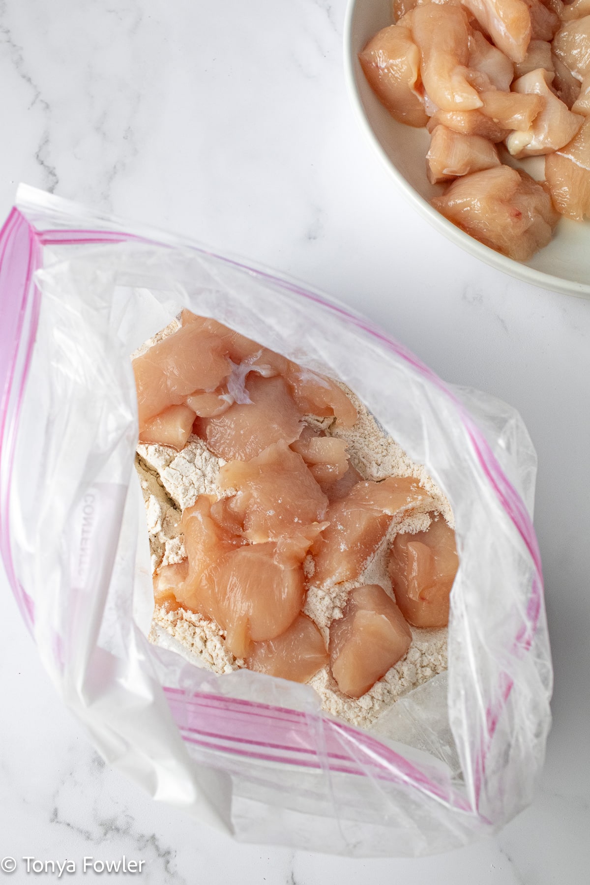 Raw chicken pieces inside a gallon bag with flour.