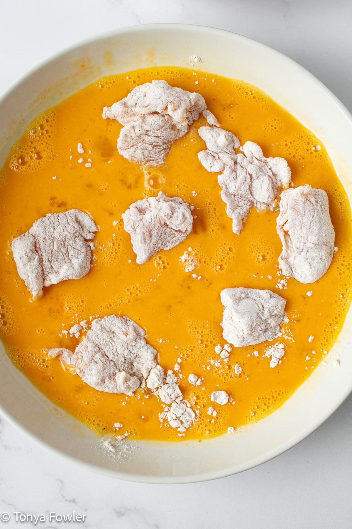 Chicken coated in flour in egg mixture.