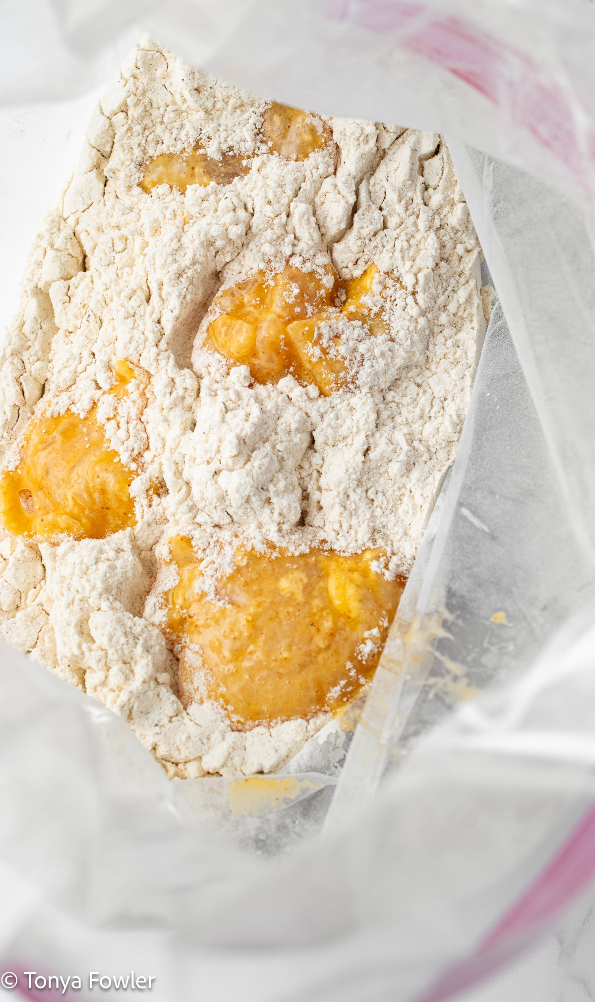 Chicken pieces coated in egg inside a bag with flour in it.