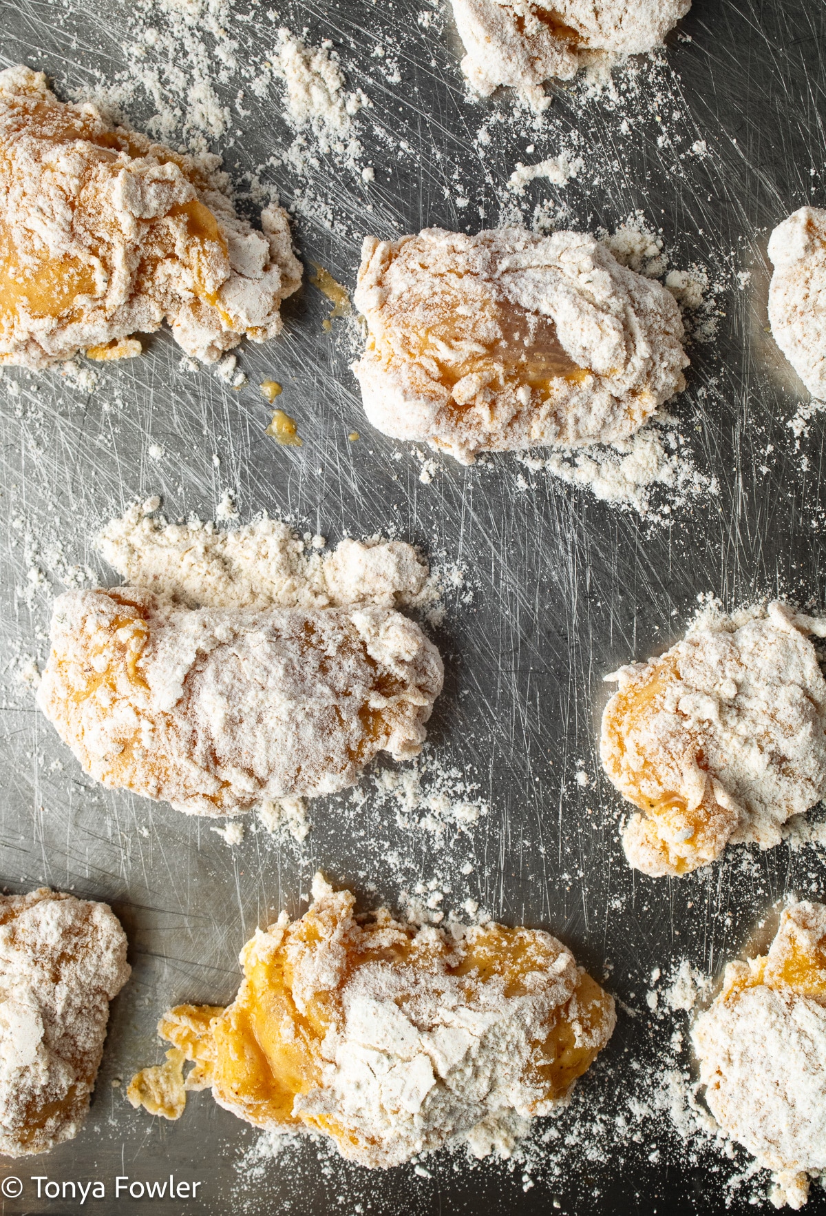 Battered and drenched chicken pieces on a metal sheet pan.