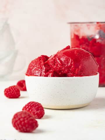 Raspberry sorbet in a bowl with fresh berries on the counter.