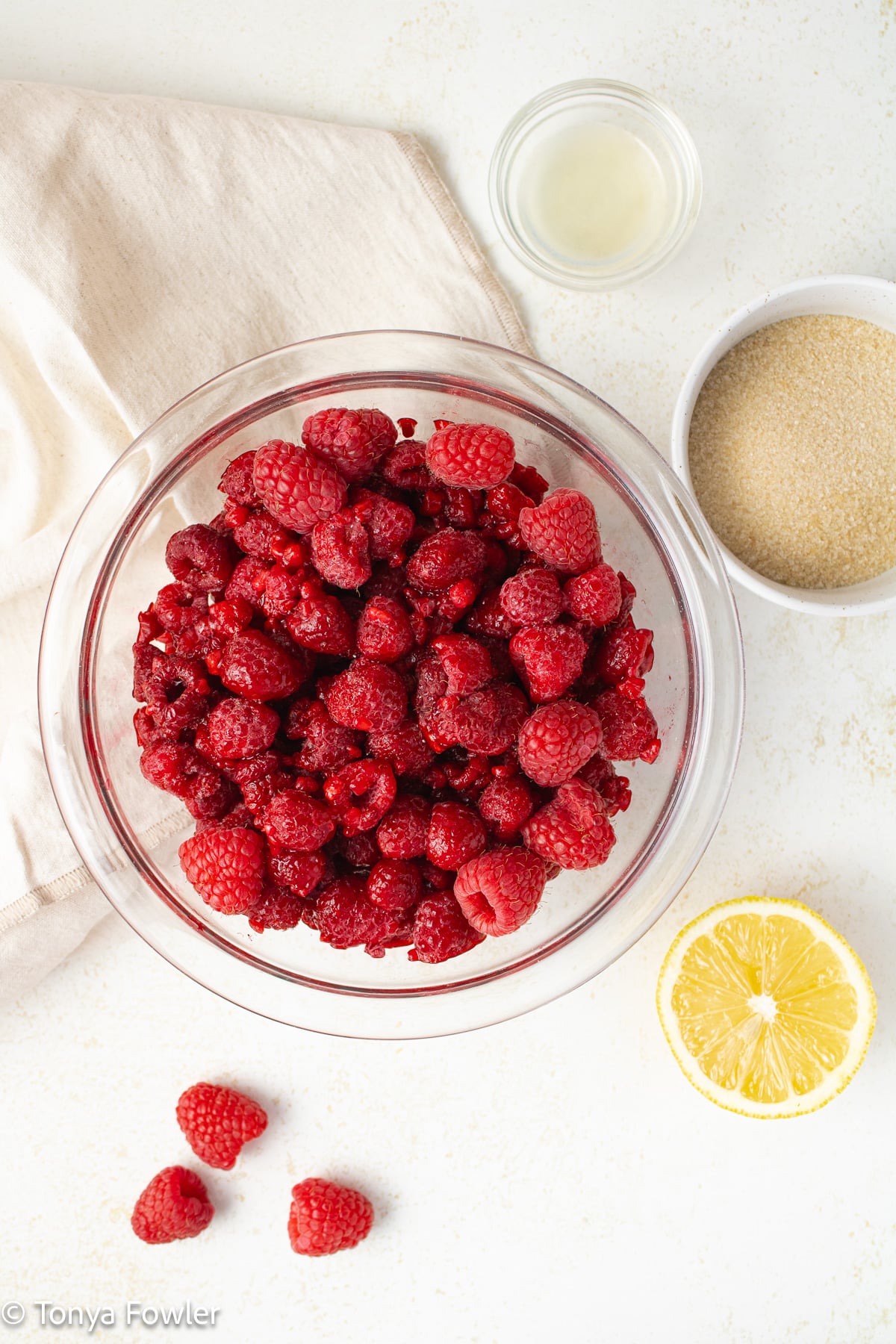Overhead image of raspberries, lemon juice and sugar on a table.