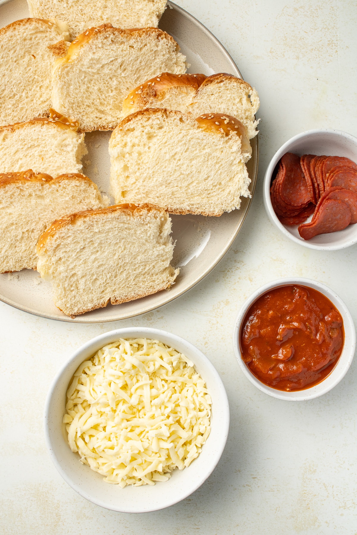 Overhead image of bread, cheese, tomato sauce, and pepperoni on a table.