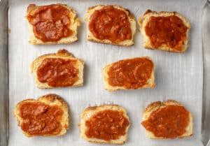 Sandwich bread slices with tomato sauce on top.