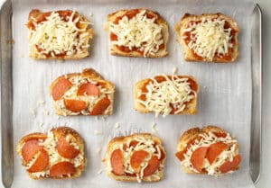 Sandwich bread topped with tomato sauce, shredded cheese, and pepperonis.