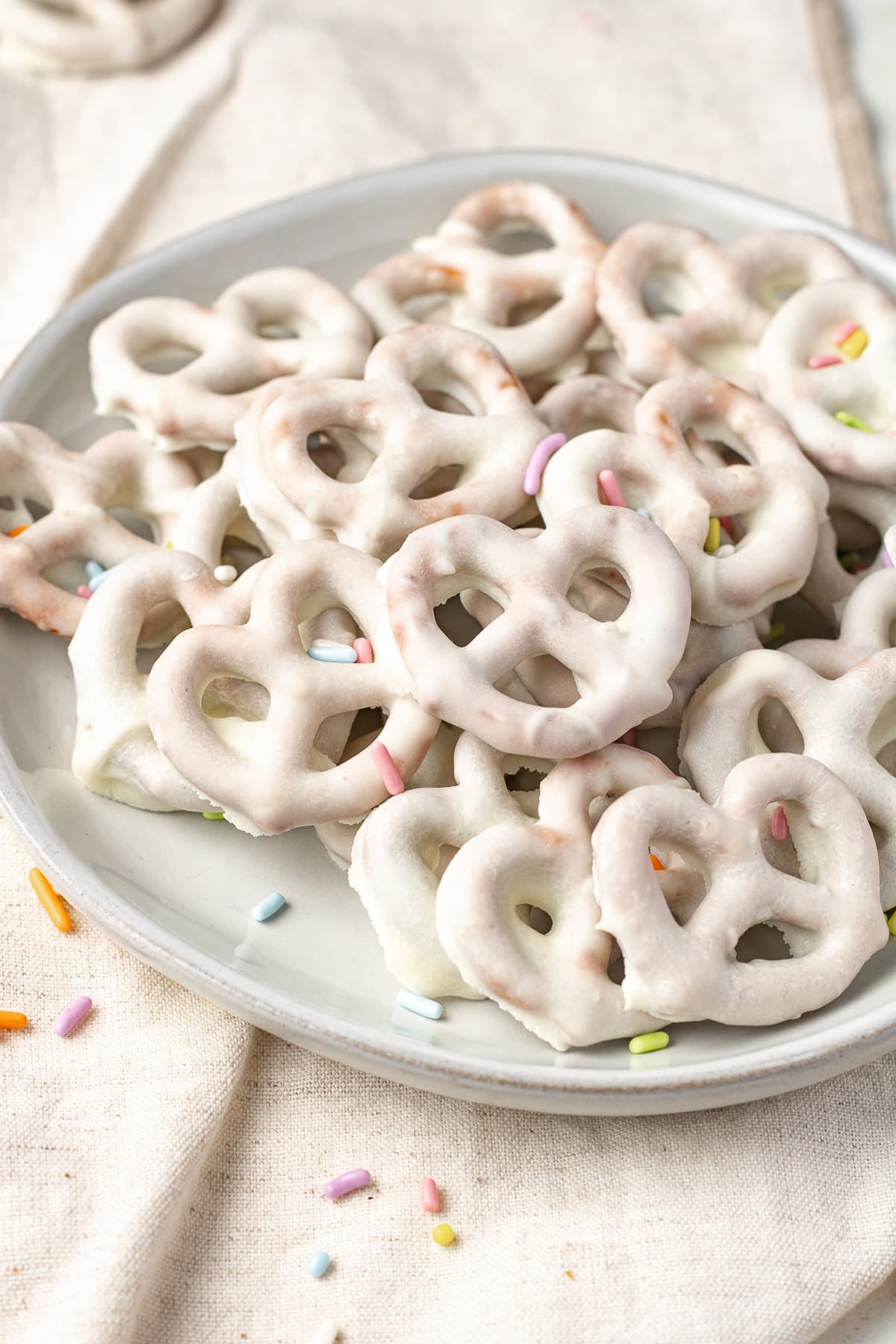 White chocolate covered pretzels on a plate with sprinkles.