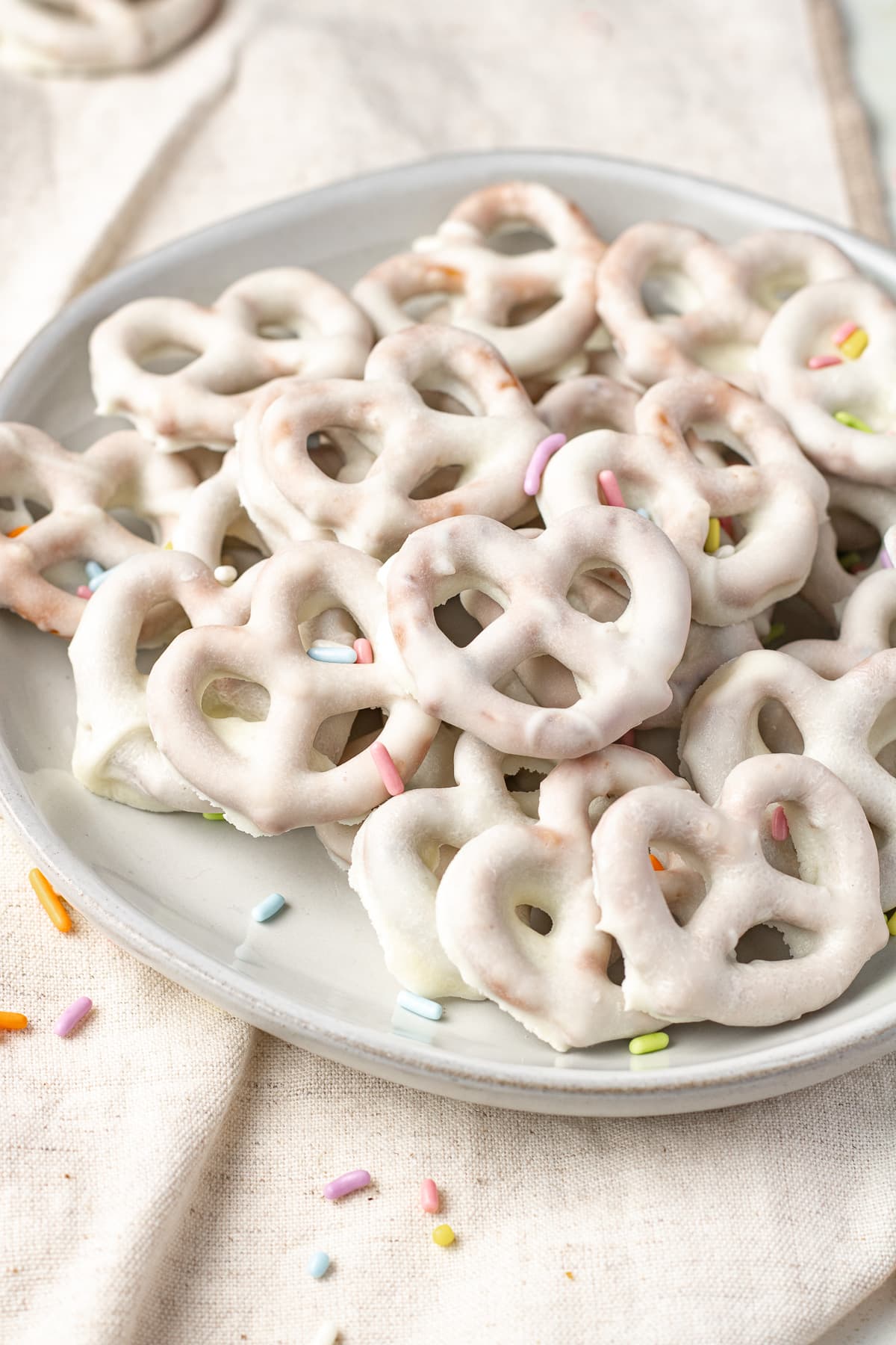 White chocolate covered pretzels on a plate with sprinkles. 