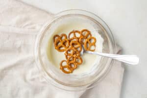 Melted white chocolate in a bowl with a few pretzels.