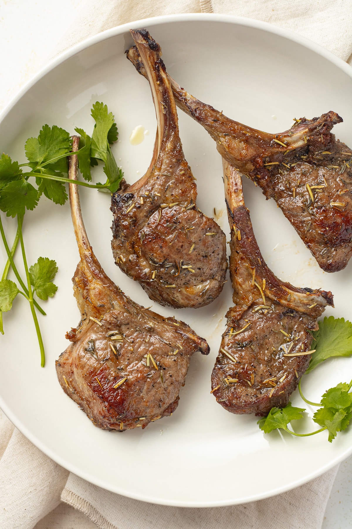 Close up image of air fryer lamb chops on a plate with herbs.