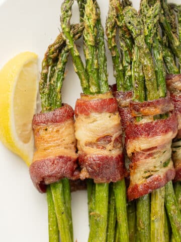 Bacon wrapped asparagus on a plate with lemon slices on a plate.