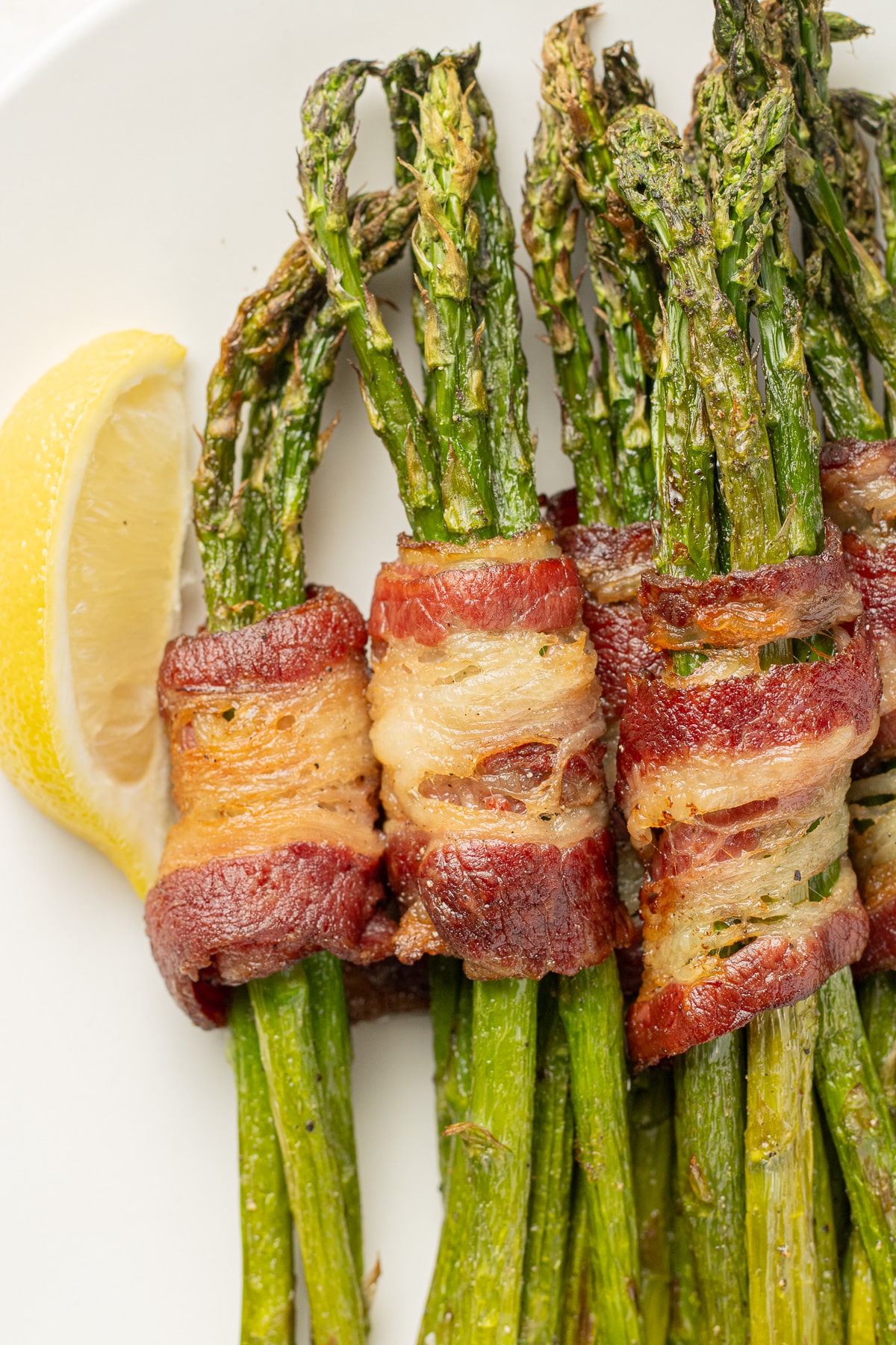 Bacon wrapped asparagus on a plate with lemon slices on a plate.