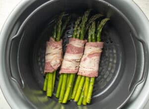 Uncooked bacon wrapped asparagus bundles in an air fryer.