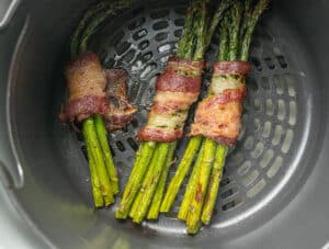 Cooked bacon wrapped asparagus in an air fryer basket.