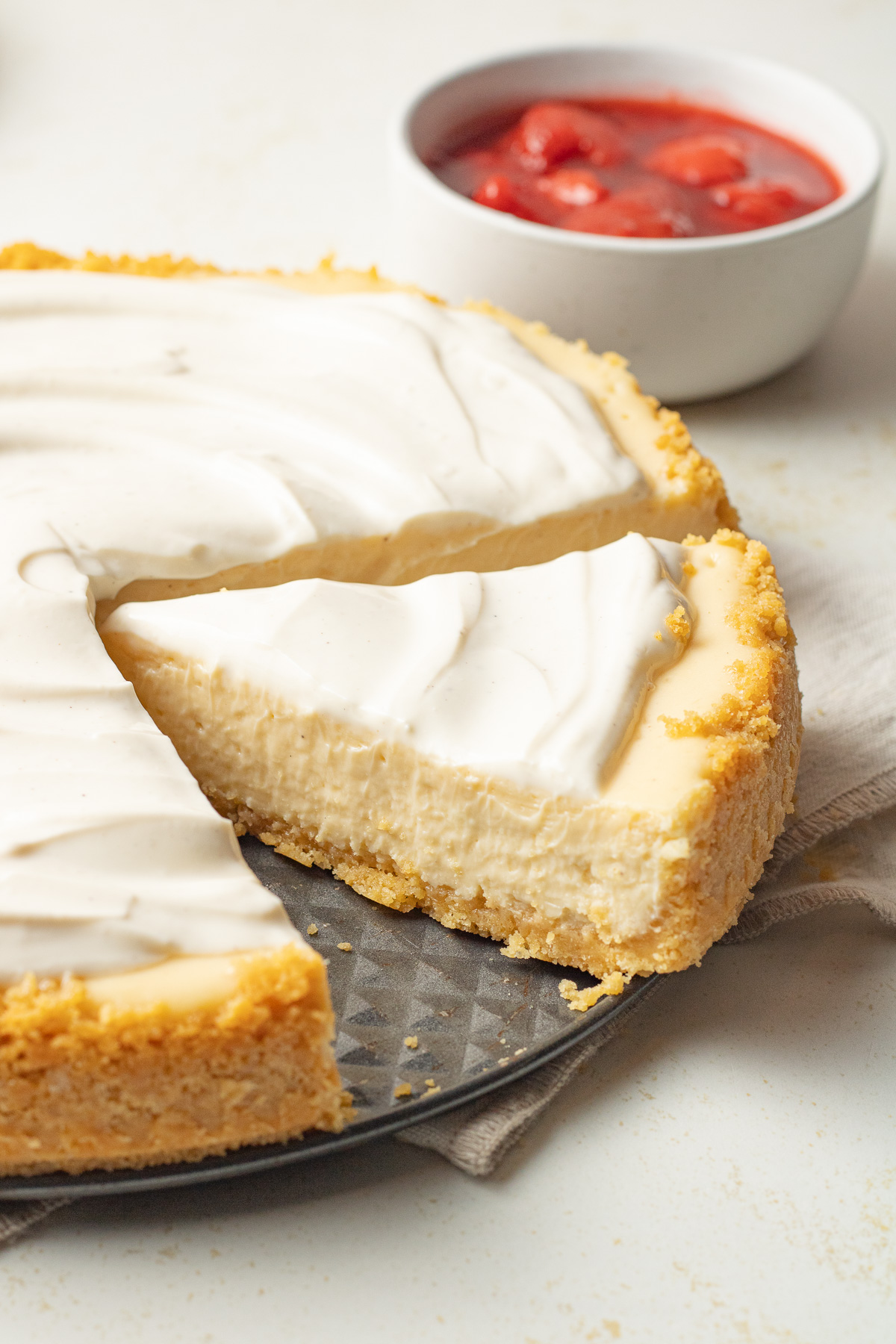 Sour cream cheesecake with sour cream topping with strawberry sauce in a bowl near by.