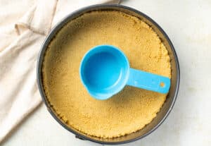 Graham cracker crust in a pan with a measuring cup.