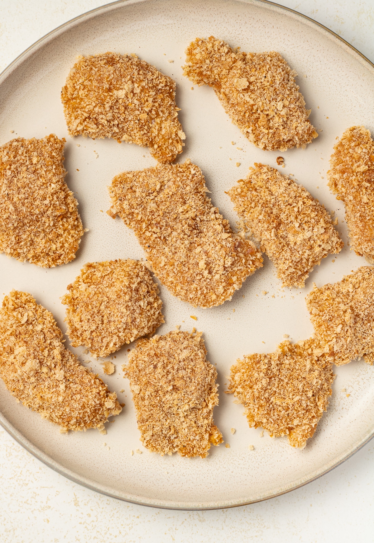 Breaded raw chicken piece on a plate.