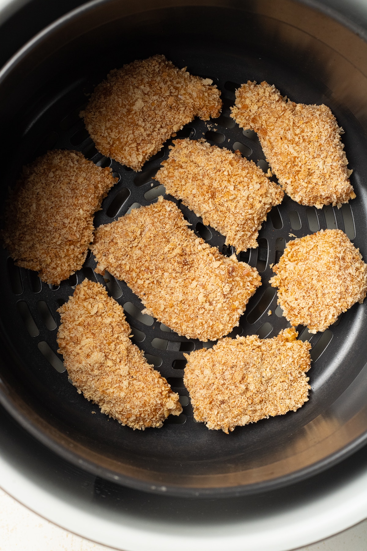 Raw breaded chicken in an air fryer basket.