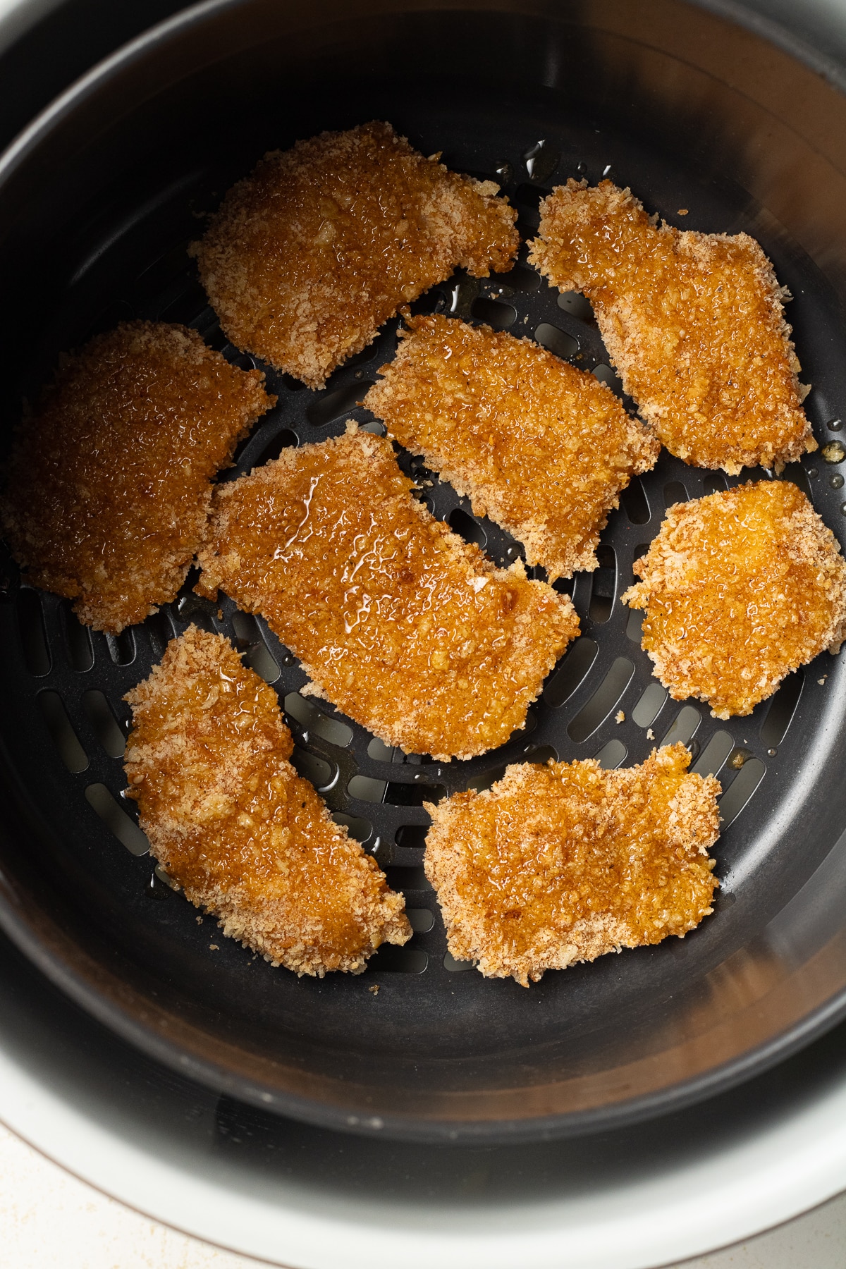Breaded chicken pieces brushed with oil in an air fryer basket. 