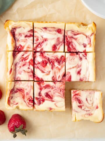 Cut cheesecake bars on parchment paper with a fresh strawberry nearby.