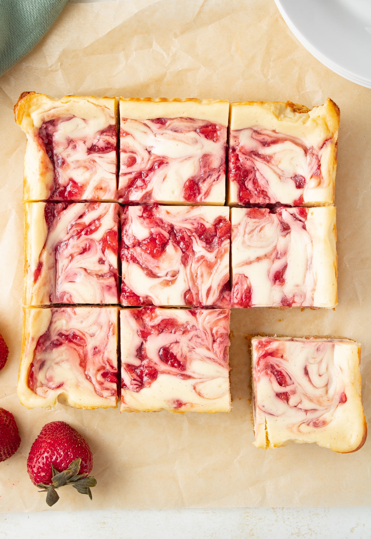 Cut cheesecake bars on parchment paper with a fresh strawberry nearby.