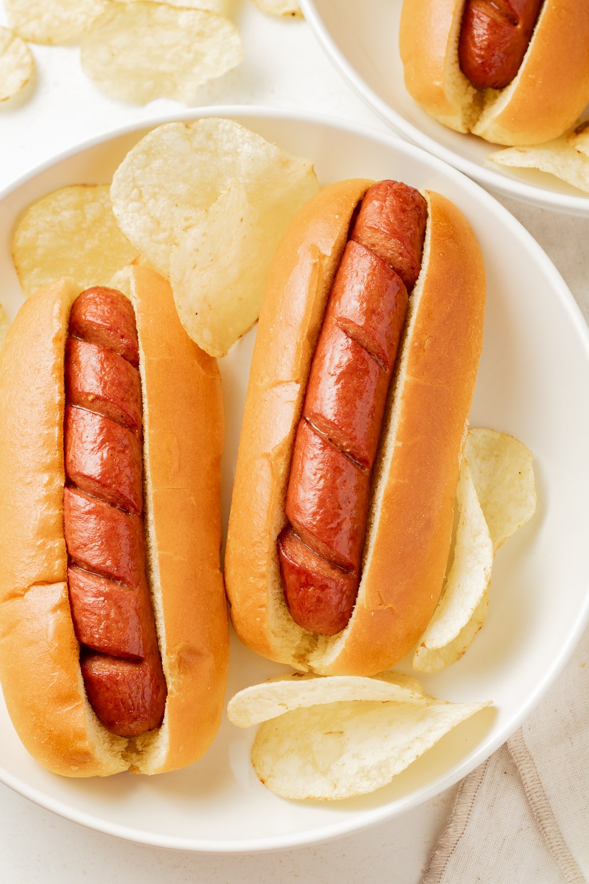 Beef hot dogs on a plate with chips.