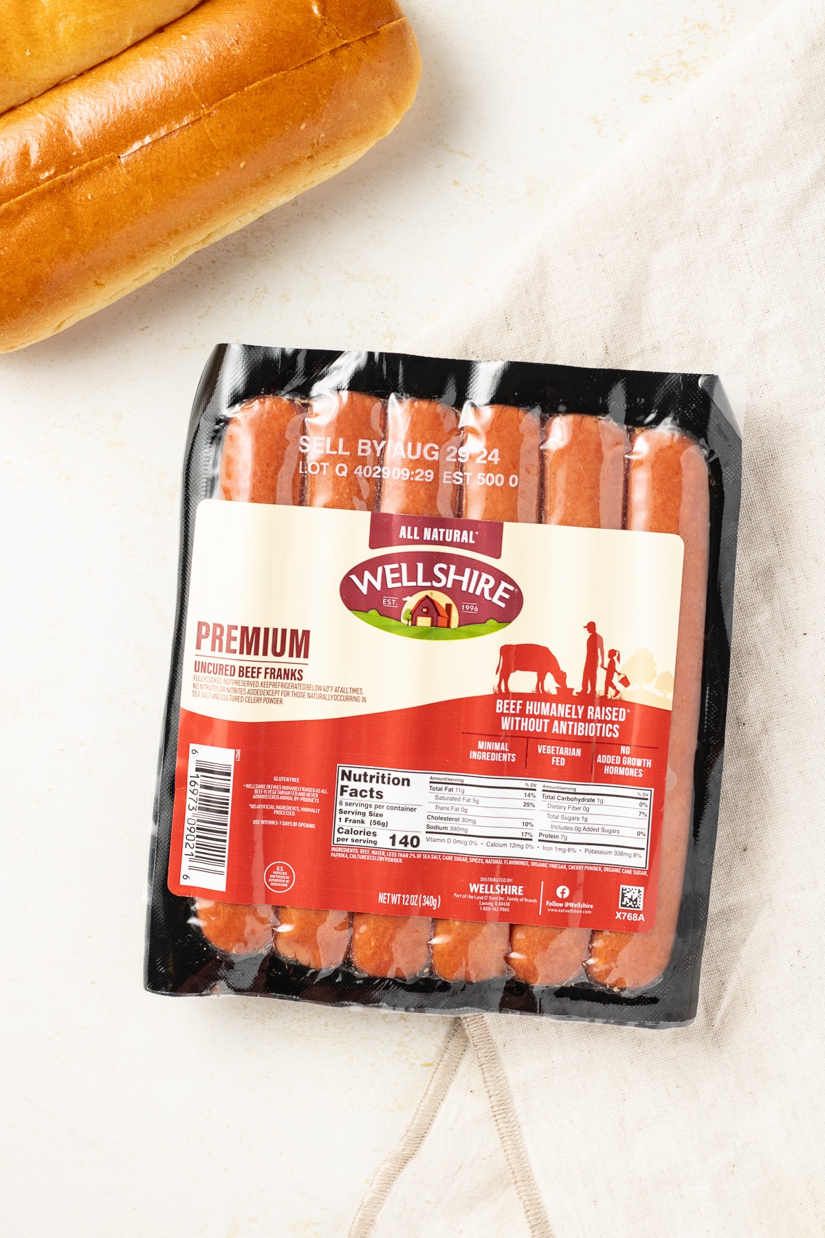 Package of beef hot dogs on a counter with buns near by.