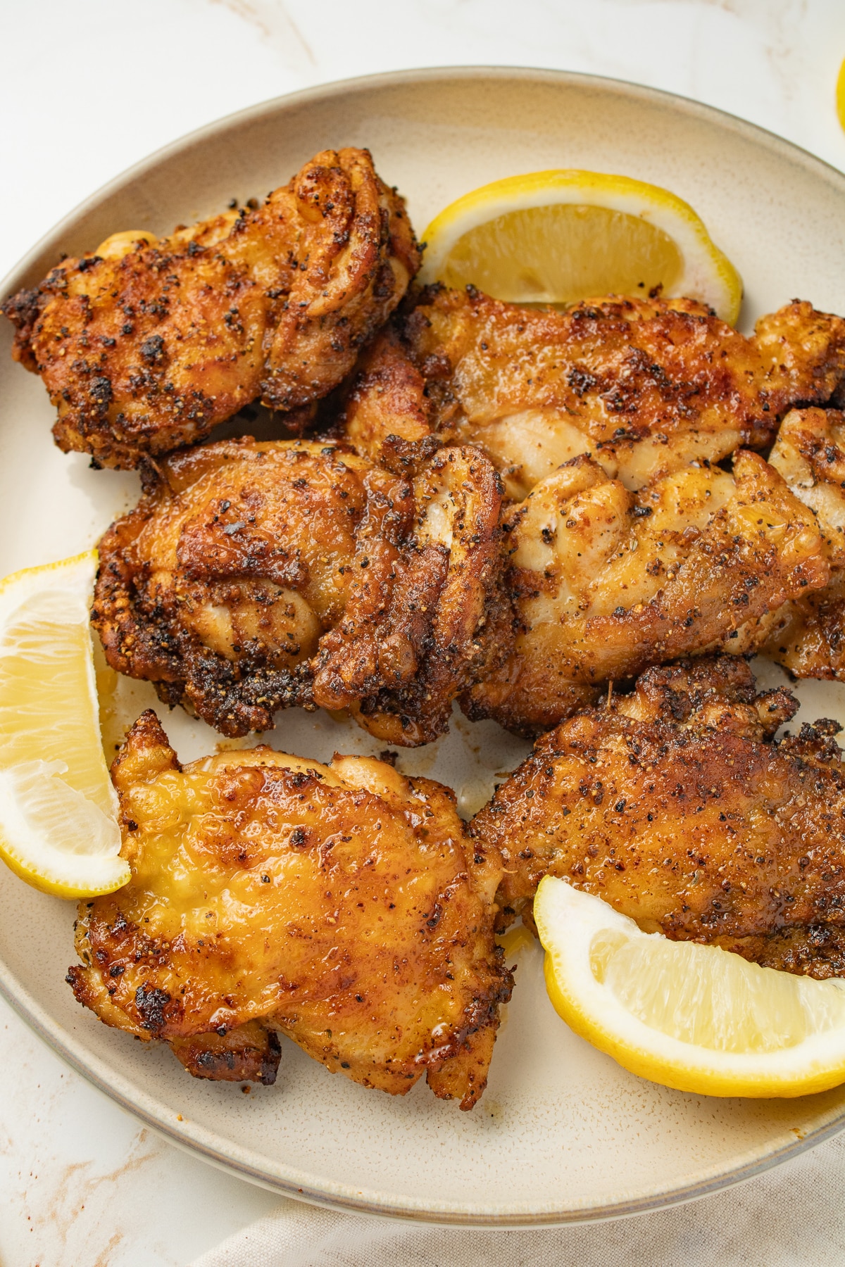 Chicken thighs on a plate with lemon wedges.