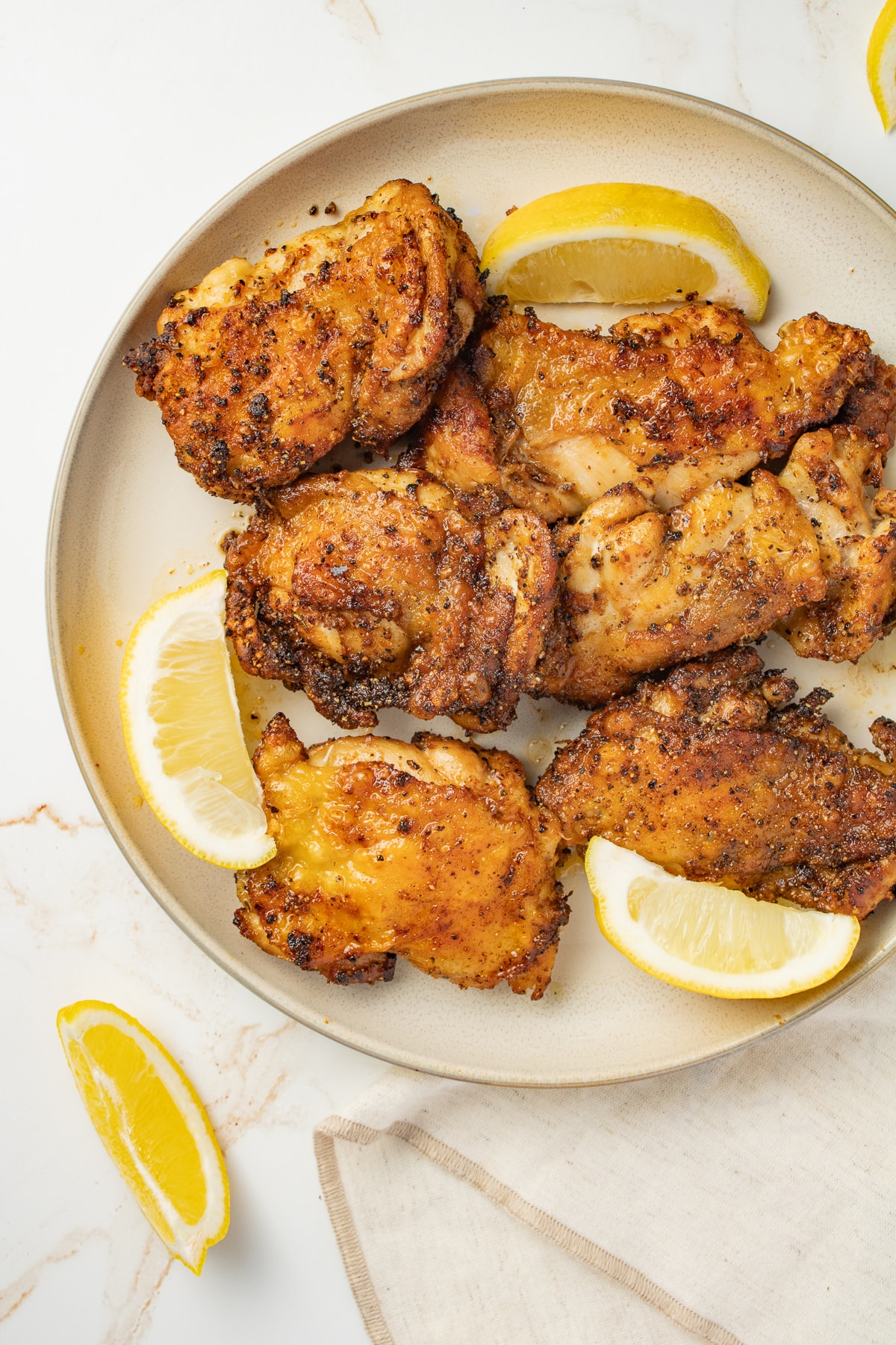Air fryer chicken thighs on a plate with lemon wedges.