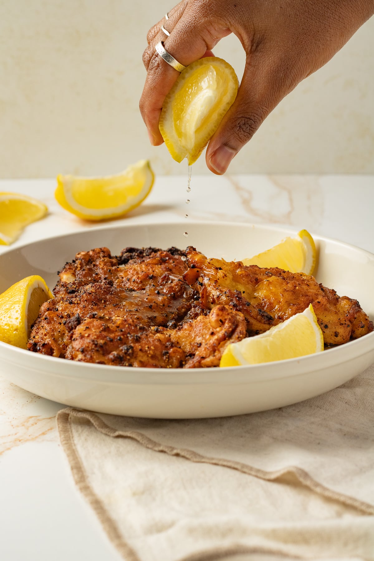 Lemon being squeezed onto a plate of chicken thighs.