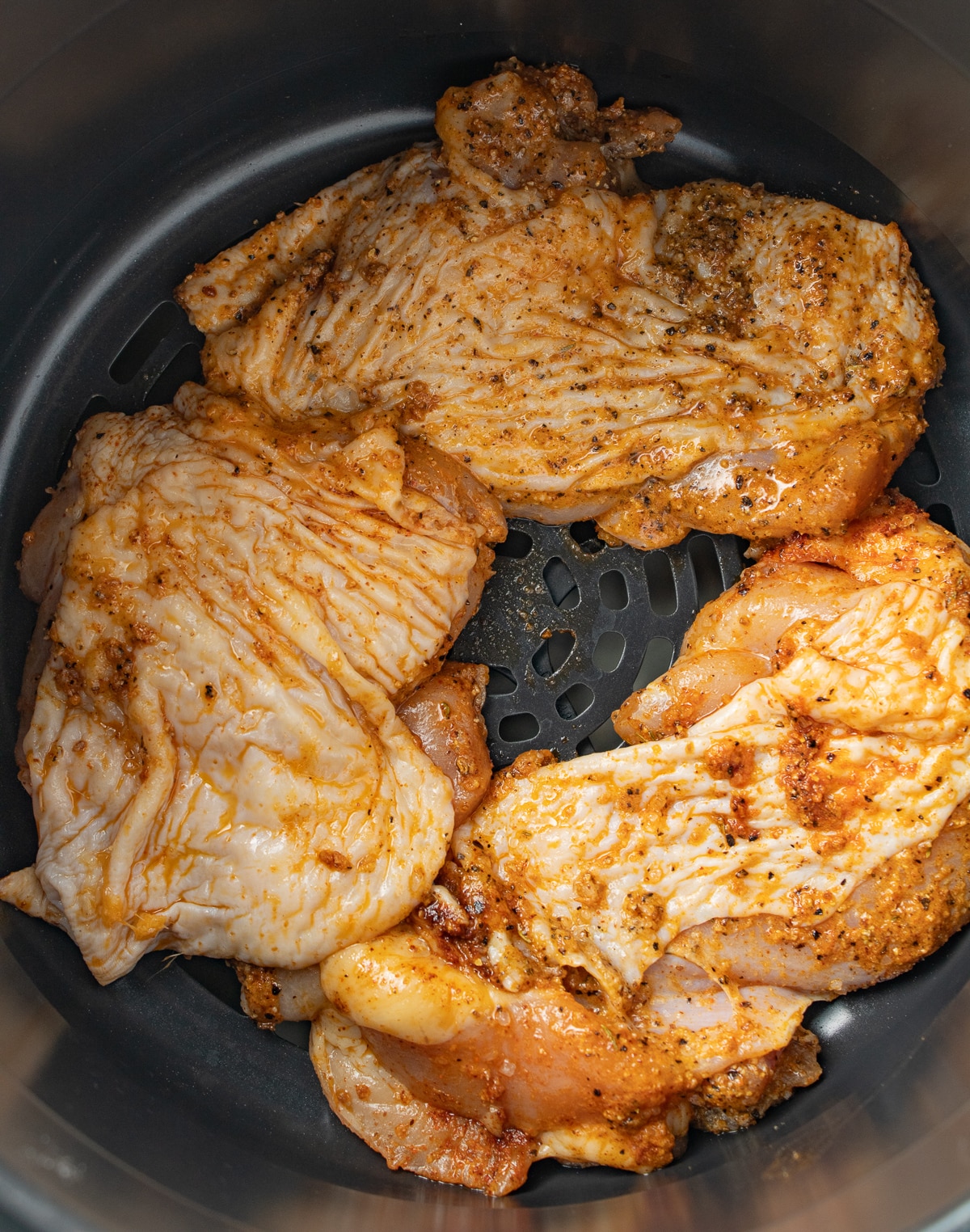 Raw seasoned chicken thighs in an air fryer basket. 