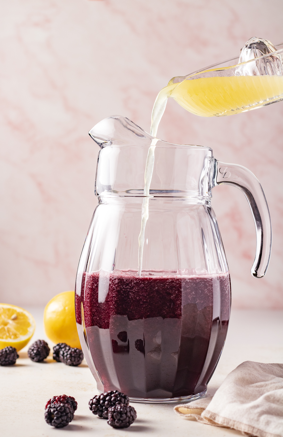 Lemon juice being poured into a pitcher with blackberry juice.