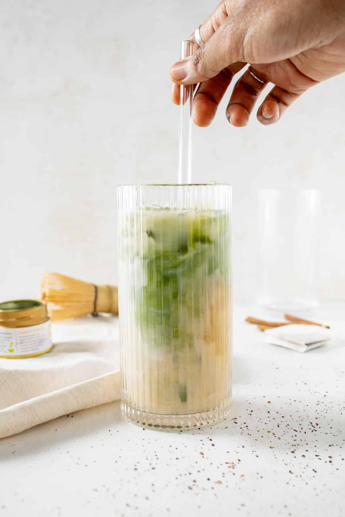 Hand stirring an iced matcha chai latte.