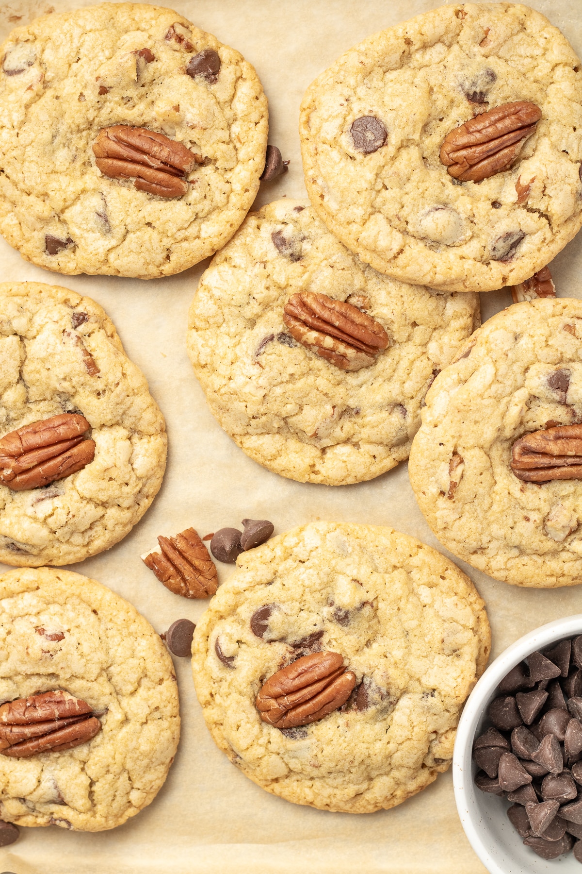 Chocolate chip cookies topped with pecans on a sheet pan.