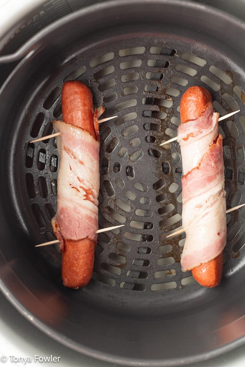 Hot dogs in an air fryer basket.